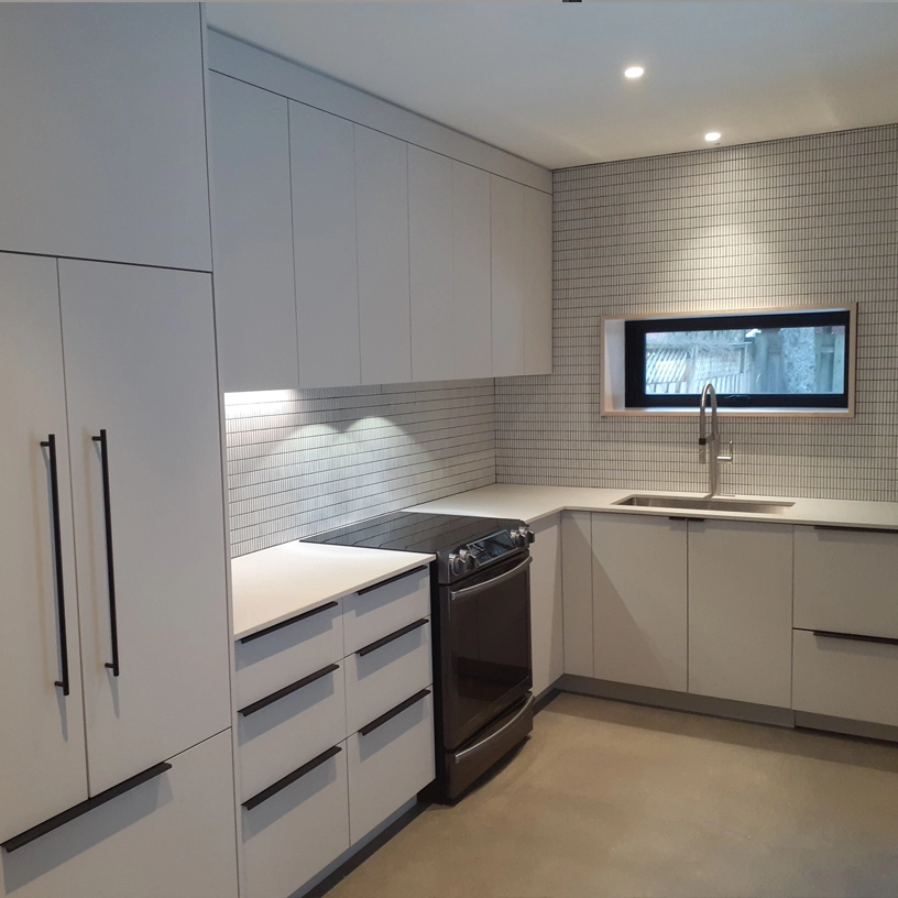 Cuisine moderne rénovée avec armoires blanches, comptoir en quartz et fenêtre horizontale